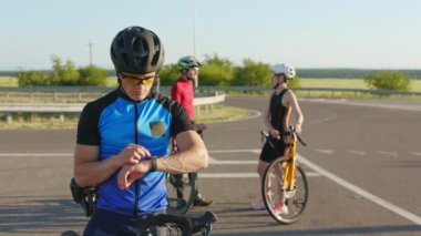 Spor giyim sektöründe profesyonel bisikletçi arka planda iş arkadaşlarıyla dışarıda dikilirken ukalalık yapıyor. Teknoloji, insanlar ve spor konsepti.