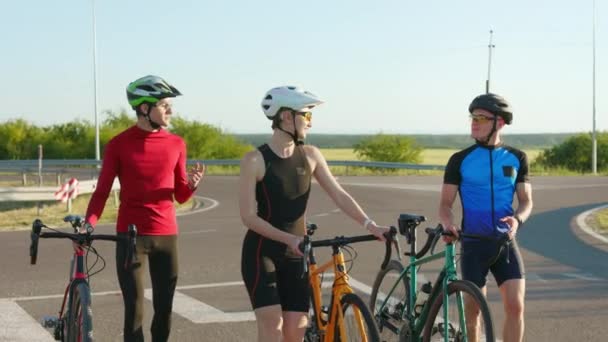 幸せな白人女性と2人の男性がカラーバイクでアスファルトの道路を歩いています スポーツウェア 安全ヘルメット メガネを身に着けているプロのサイクリスト — ストック動画