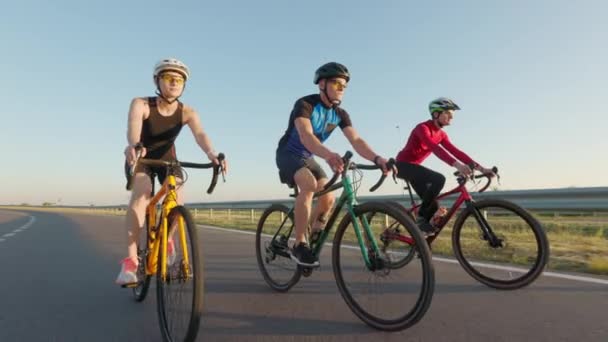 スポーツ服の白人女性と2人の男性とアスファルトの道路上の自転車に乗る安全ヘルメット プロのサイクリストの屋外トレーニング アクティブライフスタイルコンセプト — ストック動画