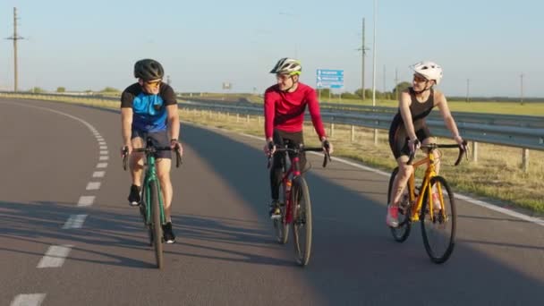 ヘルメットとメガネの3人のプロのサイクリストは 新鮮な空気に乗るためにスポーツバイクを使用しています 新鮮な空気に筋肉の白人男性と女性のトレーニング活動 — ストック動画
