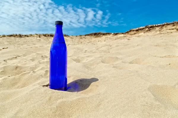 Blue water bottle standing in dry yellow sand — Stock Photo, Image