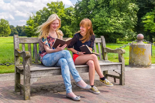 Chicas sentadas en un banco de madera en el parque leyendo libros —  Fotos de Stock