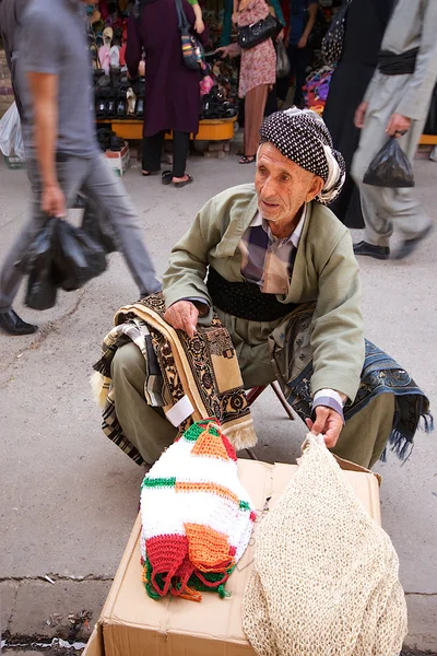 Tapestry tradesman sitting in the middle of crowded street in bazaar market. Iraq. Middle East. — Stock Photo, Image