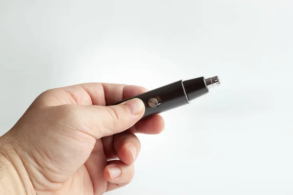 Hand holding a black nose trimmer. Close up. Isolated on a grey background.