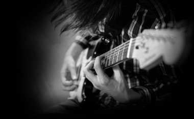 Elektro gitar çalıyor. Genç bir adam elektro gitar çalar. Siyah ve beyaz yakın çekim fotoğrafçılık.