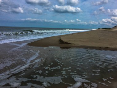 Atlantik Okyanusu 'nun güçlü dalgaları Cape Henlopen Eyalet Parkı, Lewes, Delaware' deki kumlu plaja çarpar. Mavi gökyüzünün altında birkaç bulut vardır.. 