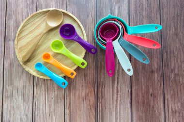 Set of plastic measuring spoon and measuring cups in various color on wooden plate in top view