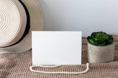 Blank white invitation card in landscape lay on knitted cloth with beach hat and pearl lace.
