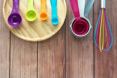 Set of plastic measuring spoon,  measuring cups and whisk in various color on wooden plate in top view