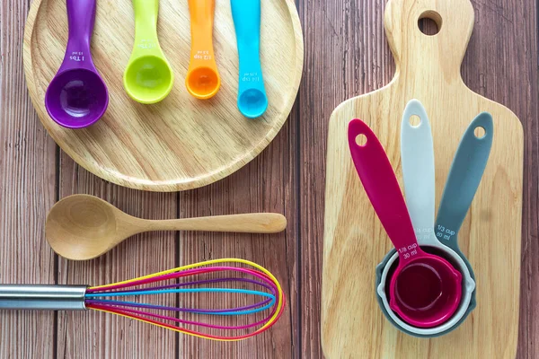 Set of plastic measuring spoon,  measuring cups and whisk in various color on wooden table in top view