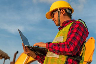 Asyalı mühendisler kazıcı tarafından yapılan toprak taşıma projesi için ekiple telsiz konuşmaları kullanırlar. Ustabaşı inşaat projesi için dizüstü bilgisayar kullanıyor. İşçi endüstrisi için makine ve ekipman.