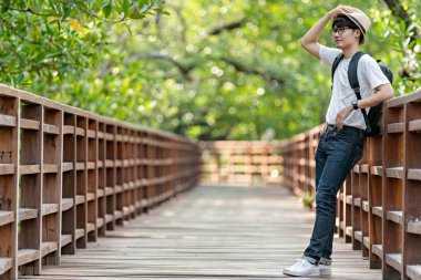 Mutlu adam mangrov ormanlarında seyahat eder. Turist gezginler sırt çantası aktivitesi için şapkalı beyaz gömlek giyerler. Asyalı adam yürüyüşe çıkmaya hazır. Tatil konsepti seyahatinde dinlenme zamanı.