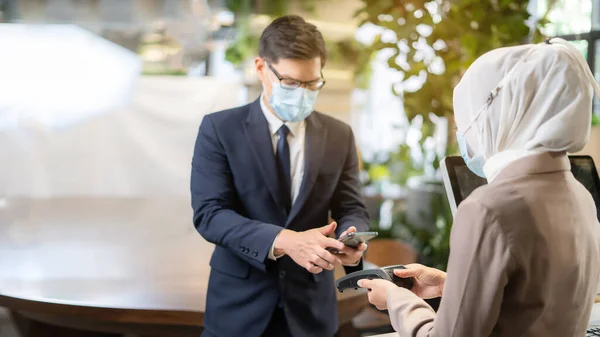 Yeni normal kavram. NFC terminali yakınında telefon tutan işadamı cep telefonu ödemesi yapıyor. Müşteri cep telefonu ile ödeme yapıyor.