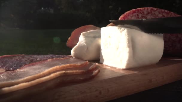 Нарезание домашнего сыра на столе для пикника с салями и прошутто — стоковое видео