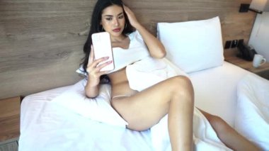 Young Sexy Asian Woman in White Underwear Lying on Bed and Looking at Smartphone 4k