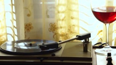 Vinyl Record on Vintage Gramophone and Glass of Red Wine in Front of Window With Old Curtains, 1960s or 1970s Home Scenery 4k