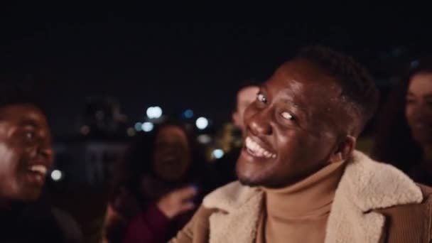 Черный мужчина танцует и улыбается с друзьями на вечеринке на крыше в городе. Высококачественные 4К кадры — стоковое видео