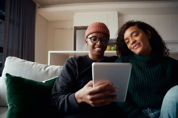Junges erwachsenes Paar, multiethnisch, sitzt mit Tablet auf Sofa in moderner Wohnung — Stockfoto