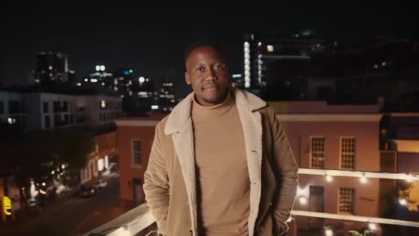 Zwarte man staat op een dak in de stad, terloops en glimlachend. Hoge kwaliteit 4K beeldmateriaal — Stockvideo