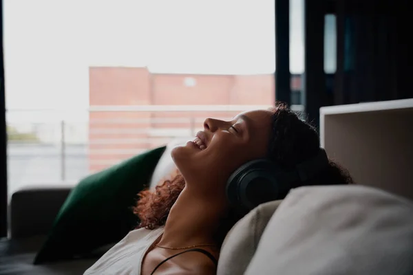 Çok ırklı bir kadın yatakta rahatlarken mutlu bir şekilde gülümseyen müzik dinliyor.