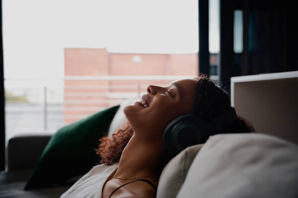 Multi-ethnic female relaxing back on bed while listening to music smiling happily — Stock Photo, Image