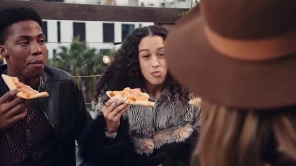 Mujer multiétnica comiendo pizza y charlando con diversos grupos de amigos adultos en una azotea al atardecer en la ciudad — Vídeo de stock