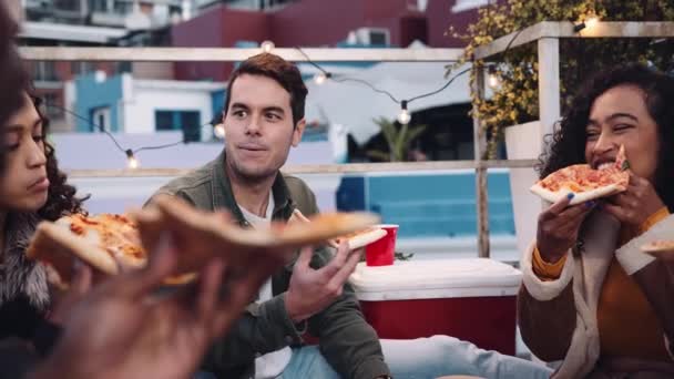 Wieloetniczna kobieta, biały mężczyzna i zróżnicowana grupa dorosłych przyjaciół jedzących pizzę i towarzysko na dachu o zmierzchu — Wideo stockowe