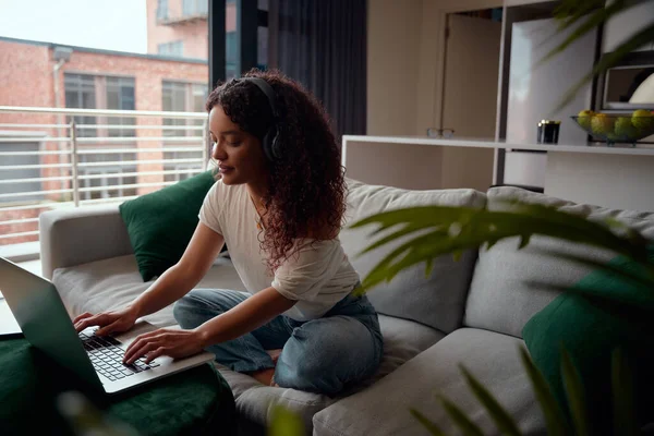 Inhoud multi-culturele vrouw op haar laptop zittend op de bank tijdens het luisteren naar muziek — Stockfoto