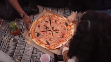 Çok ırklı bir grup yetişkin arkadaş açık hava partisinde pizza yiyorlar.