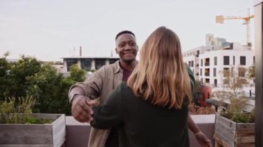 Zenci erkek, şehrin alacakaranlığında çatıdaki bir partide beyaz bir bayanı selamlıyor.