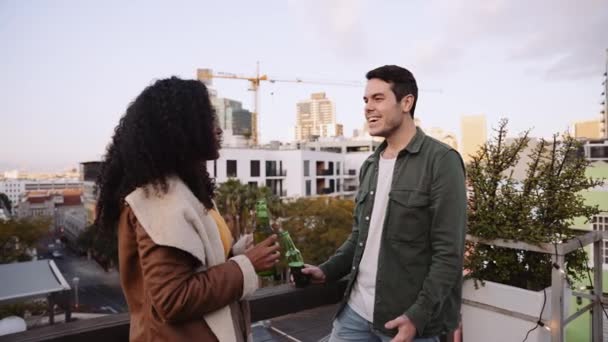 Caucasian male and Multi-cultural female socializing with drinks on a rooftop in the city at dusk — Stock Video