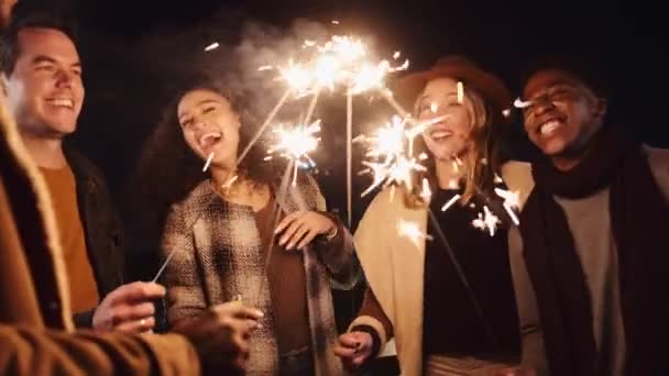 Diverso grupo de amigos rindo e iluminando seus brilhos ao ar livre durante a noite. Imagens 4K de alta qualidade — Vídeo de Stock