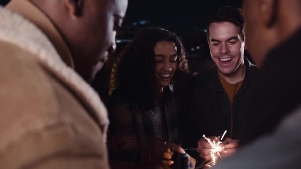 Groupe multiethnique d'amis allumant leurs étincelles et célébrant lors d'une fête sur le toit dans la nuit. Images 4K de haute qualité — Video