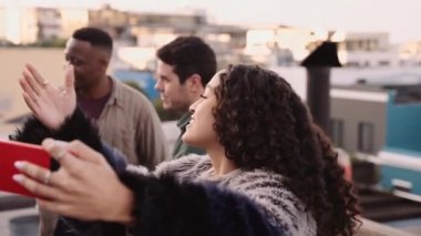 Çok kültürlü bir kadın, arkadaşlarını çağırıyor. Akşam karanlığında şehrin çatısında selfie çekecekler.