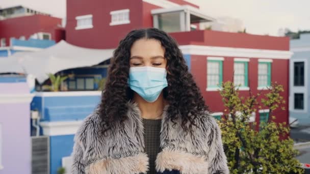 Mixed race adult female taking mask off and smiling at camera on a rooftop in the city at dusk. Colorful cityscape in background — Stock Video