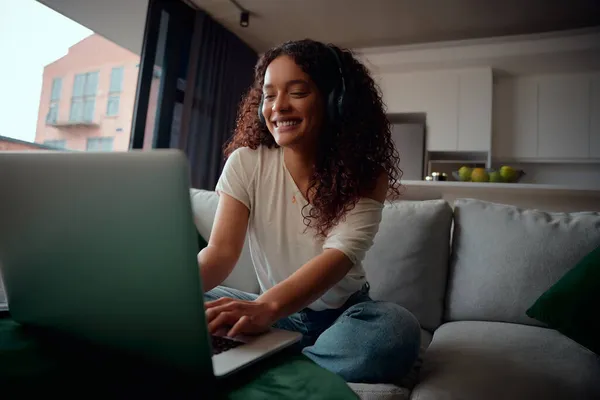 Mulher multi-étnica excitada em seu laptop sentado no sofá enquanto ouve música — Fotografia de Stock