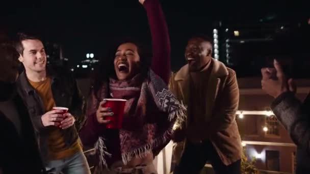 Мультикультурная женщина танцует со своими друзьями на вечеринке на крыше в городе с напитками — стоковое видео