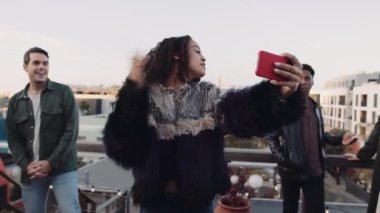 Kadın, çatıdaki akıllı bir telefondan selfie çekmek için farklı bir arkadaş grubunu arıyor. Yüksek kalite 4K görüntü.