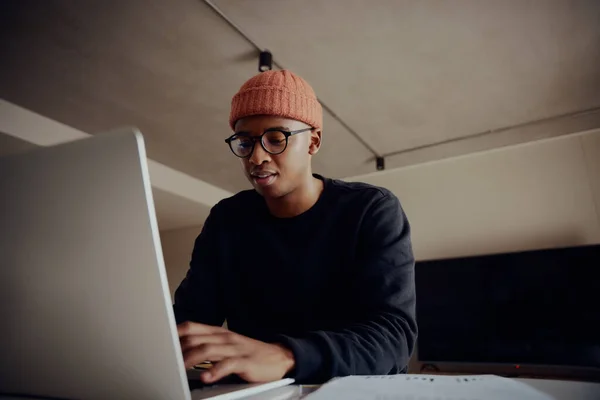 Homem preto digitando no laptop enquanto sentado no balcão da cozinha. Trabalho jovem adulto a partir de casa — Fotografia de Stock