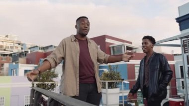 Zenci erkek, çeşitli yetişkin arkadaş gruplarını çağırıyor. Alacakaranlıkta çatıdan manzaraya bakmak için. Bir grup arkadaş gülümsüyor. 