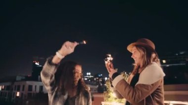 Çok kültürlü ve beyaz bir kadın, gece vakti şehrin çatısında maytaplarla dans ediyor.. 