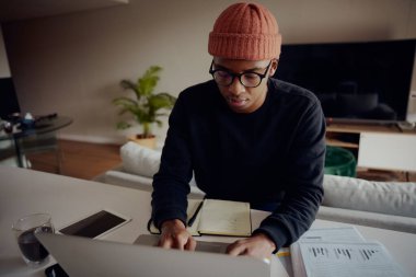 Laptopuyla evde çalışan Afro-Amerikalı bir erkek. Kağıt ve kalemle Afrika kökenli Amerikalı erkek planlaması haftası