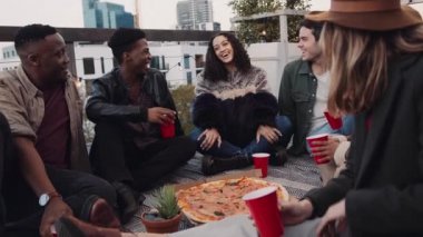 Çeşitli yetişkin arkadaşlar kışın gün batımında çatıda oturup pizza yiyorlar. Yüksek kalite 4K görüntü
