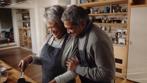 Donna anziana multiculturale che cucina in cucina, accompagnata dal marito che le dà un abbraccio. Filmati 4k di alta qualità — Video Stock