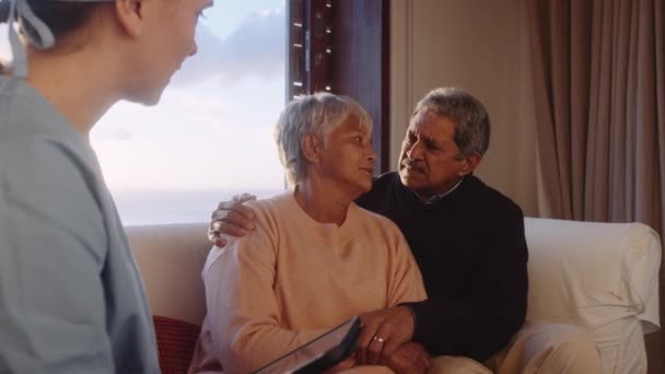 Profesional médico que utiliza la tableta para explicar la retroalimentación negativa de las exploraciones a una pareja de ancianos en casa — Vídeos de Stock