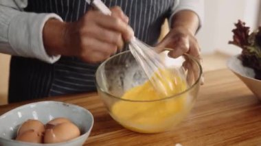 Modern mutfakta yumurta çırpan çok kültürlü yaşlı bir adam. Eller yukarı.