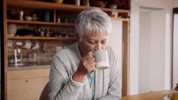 Çok kültürlü yaşlı bir kadın kahvesini yudumluyor, kamerayı fark ediyor ve modern mutfakta gülümsüyor. — Stok video