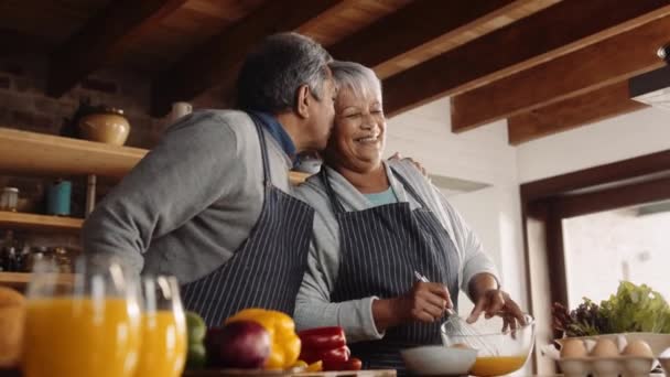 Blandad ras äldre par matlagning tillsammans i modernt kök. Maken kysser sin fru — Stockvideo