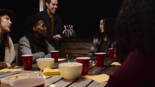 Caucásico macho presentando pastel de cumpleaños a multi-cultural chica de cumpleaños en una mesa con sus amigos — Vídeo de stock