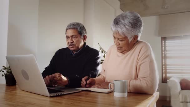 Multi-culturale coppia anziana discutendo piani utilizzando computer portatile insieme, seduto al bancone della cucina — Video Stock